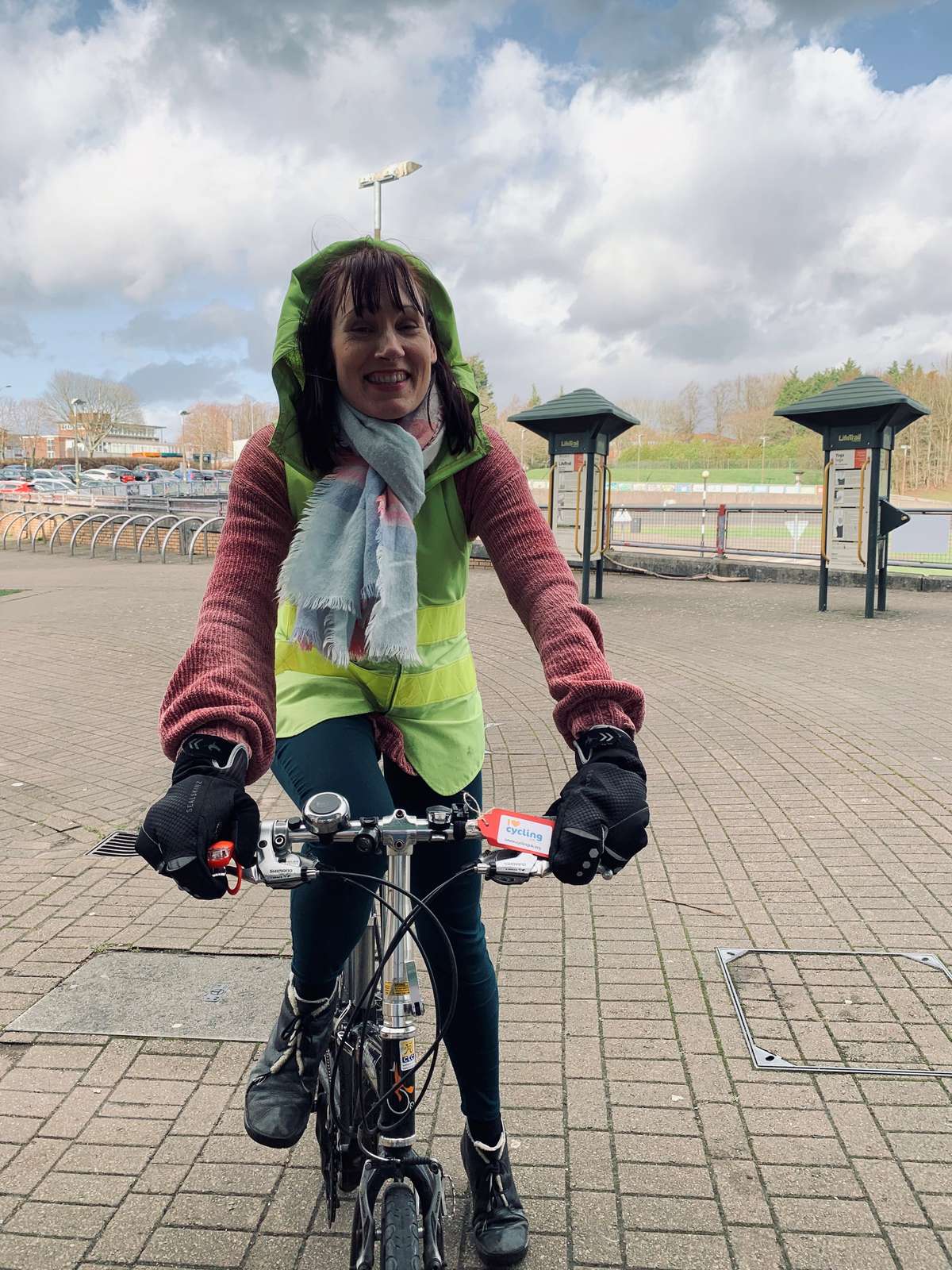 A woman facing head on to the camera standing with one foot on the floor and another on the pedal of her bicycle