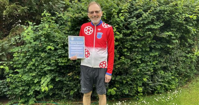 A man proudly displays a certificate in front of a green hedge  Photo by Reading CTC