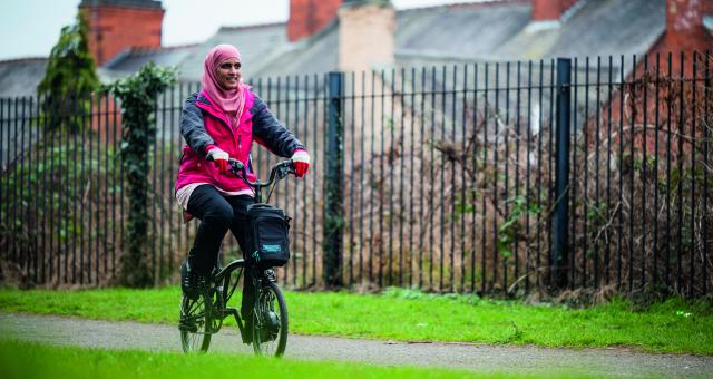 A woman in a headscarf is cycling on a paved path on an e-bike