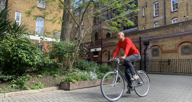 A man is cycling on a cobble path. It’s a fixie bike and he’s wearing normal clothes: a red sweater and black jeans