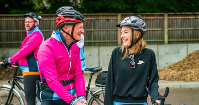 Two people, an older man and younger woman, are standing with their bikes, looking at each other and smiling