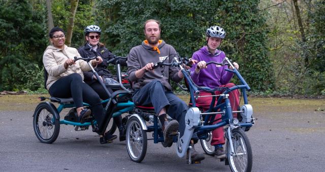 Four people on a non-standard cycle all peddling together on the pavement