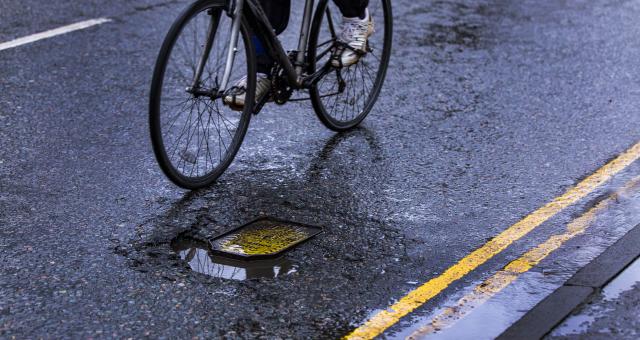 A person on a bicycle is riding around a pothole in the road