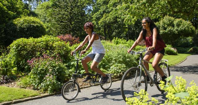 Two women cycling on a path out in the sun © Joolze Dymond