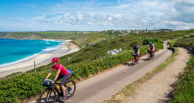 3 cyclists on the West Kernow Way route in Cornwall cycling on a path next to the sea