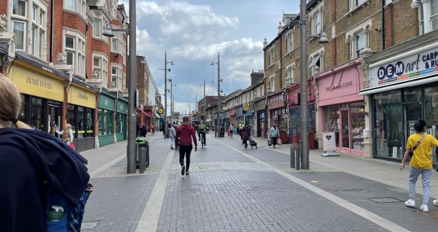 A busy high street with people walking and cycling and carrying shopping bags. The street is only open to cycling and walking