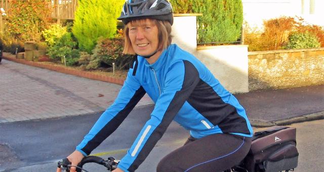 A woman is riding a black touring bike. She's wearing cycling kit and a helmet