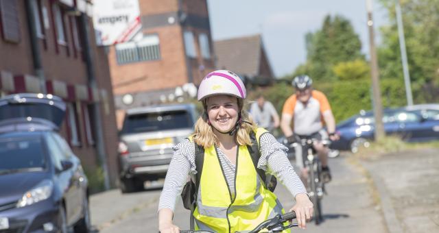 A woman smiling and cycling along through a quiet street