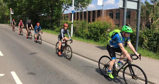 Six cyclists are riding along an urban road in single file