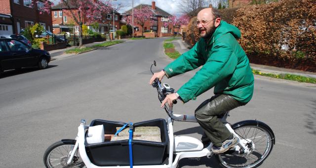 A man in a green puffa jacket and green trousers is riding a white e-cargo bike carrying 110kg of concrete