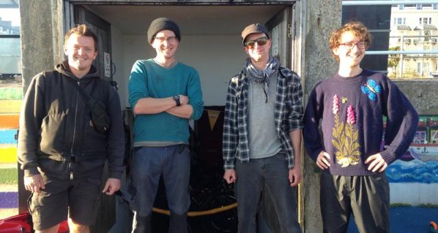 Four men stand in front of a shelter with a sign above it which says Labyrinth