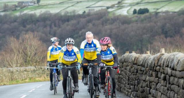 Four cyclists riding in two pairs up a hill with a stone wall to their left