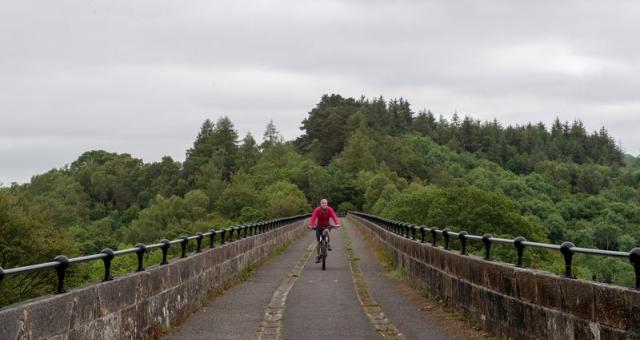 An image showing a distant woman in pink on a bicycle riding across a bridge toward the camera 