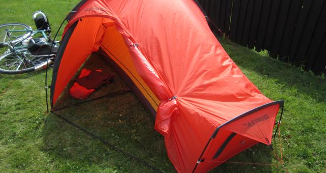 A bright orange 1-person tent is pitched up on grass