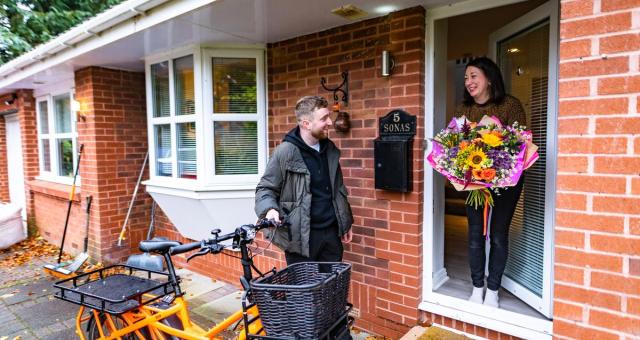 man with cargo bike making delivery of flowers to woman at door of house