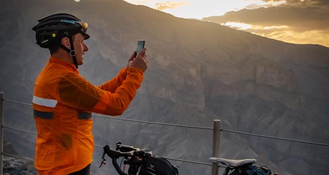 A man in cycling kit is standing next to his bike taking a photo