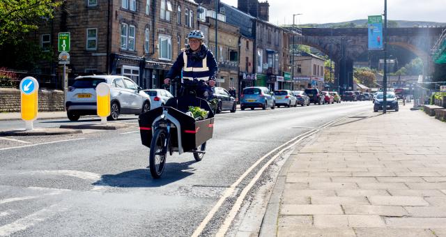 Person rides an e-cargo bike on the road, buildings in the background