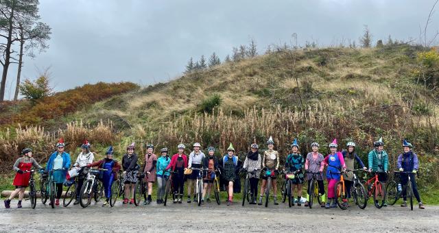 A group of women about to ride their bikes in the forest wearing party dresses.