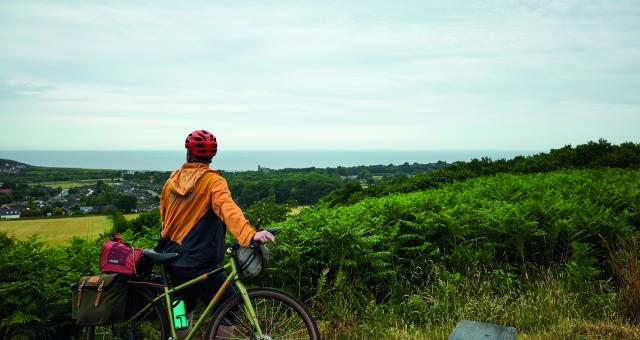 A man wearing cycling gear leaning on his bicycle overlooks a cove