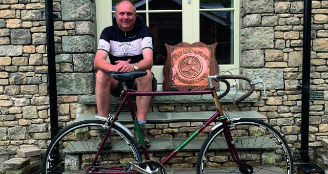 A man sits on a window sill behind his vintage bicycle. A winged-wheel CTC plaque is beside him