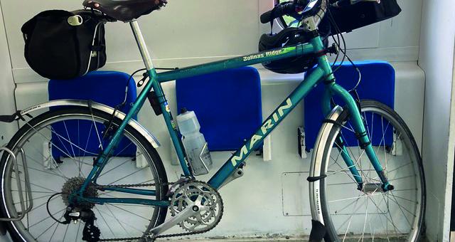 A bicycle leans against folded chairs on a train in the bicycle carriage. It's carrying rear and front rack bags