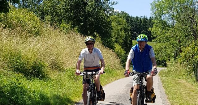 A man and a woman are cycling towards the camera on a quiet road in warm conditions