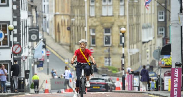 A woman wearing a red t-shirt pedals uphill on a sunny day in England