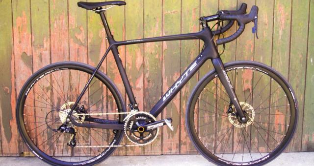 A matt purple road bike is leaning against a wooden fence