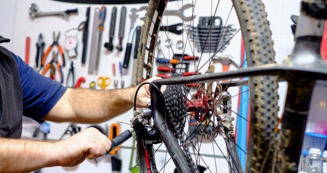 A bike is hanging on a work stand. A person is adjusting the derailleur