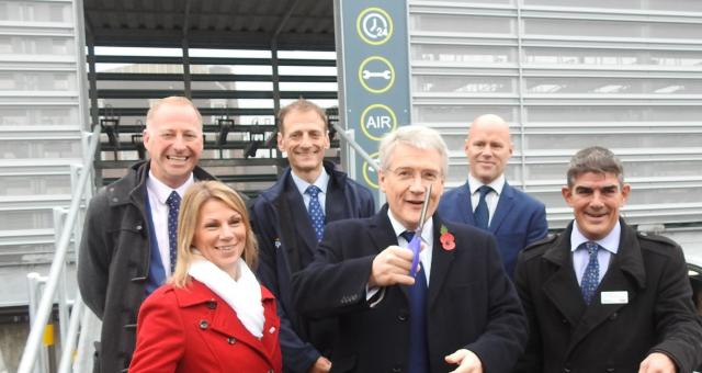 A group of people are standing in front a building with a Cycle Hub sign above the door. A man at the front is cutting a red ribbon