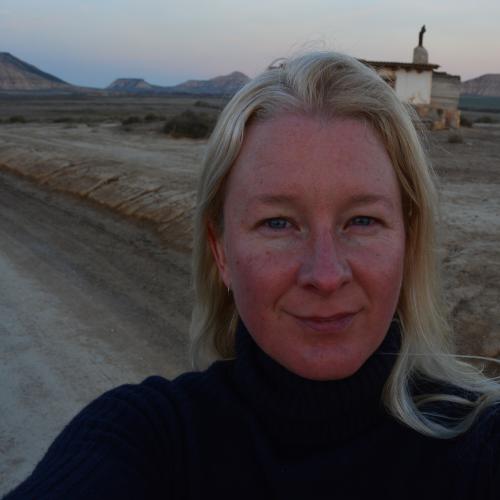 Close-up headshot of Anna in a desert landscape. She is wearing a dark jumper. 